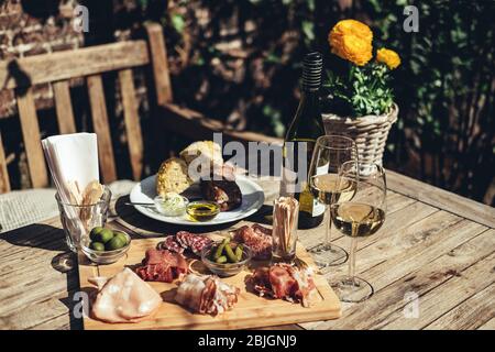 Salumi serviti con vino bianco all'aperto. Un piatto di prosciutto e pancetta affettare con sottaceti su una tavola di legno Foto Stock