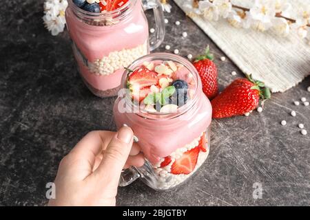 Donna mano tenendo delizioso parfait con frutta in vaso sul tavolo Foto Stock