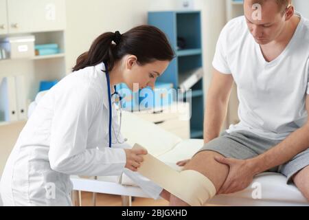 Ortopedist applicando bendaggio sul ginocchio del paziente in clinica Foto Stock