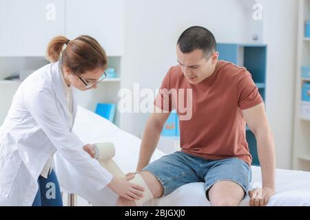 Ortopedist applicando bendaggio sul ginocchio del paziente in clinica Foto Stock