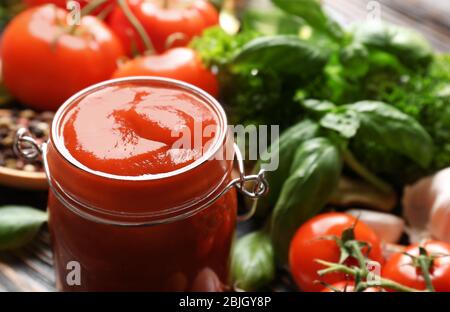 Composizione del ketchup in vaso e ingredienti su fondo di legno Foto Stock