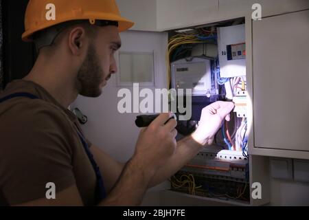 Giovane elettricista con torcia vicino alla scatola di commutazione in camera oscura Foto Stock