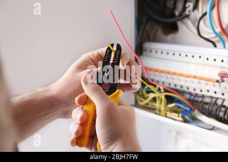 Giovane elettricista che scuoii un filo in stanza luminosa Foto Stock