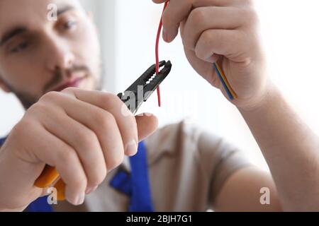 Giovane elettricista che scuoii un filo in stanza luminosa Foto Stock