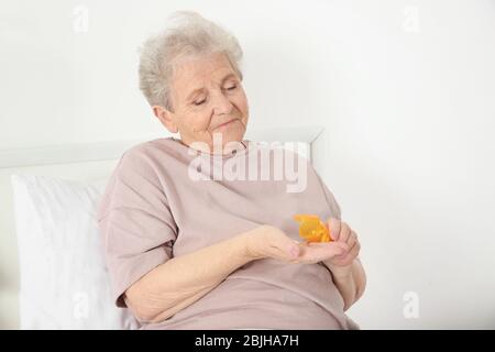 Donna anziana che va a prendere la medicina mentre siede sul letto a casa Foto Stock