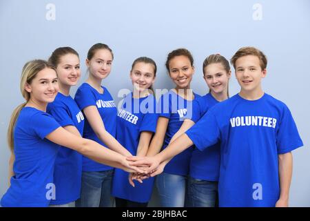 Gruppo di volontari che mettono le mani insieme come simbolo di unità, su sfondo colorato Foto Stock