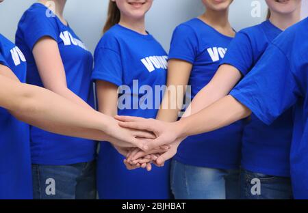 Gruppo di volontari che mettono le mani insieme come simbolo di unità, su sfondo colorato Foto Stock