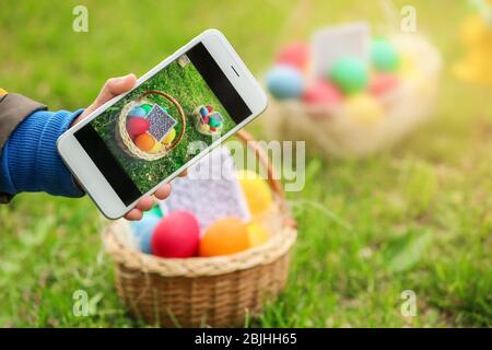 Bambino che scandisce il codice QR nel cestino con uova colorate al parco. Concetto di caccia pasquale Foto Stock