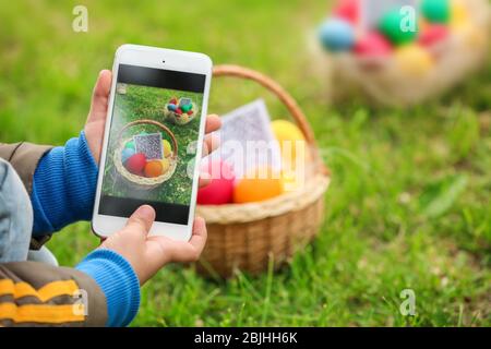 Bambino che scandisce il codice QR nel cestino con uova colorate al parco. Concetto di caccia pasquale Foto Stock