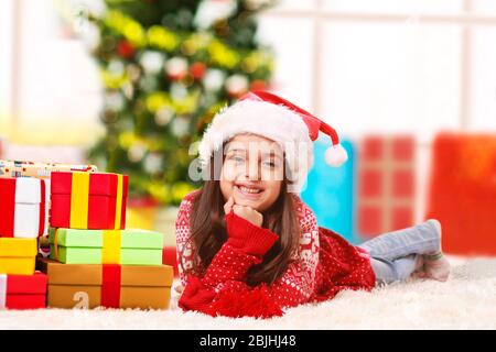 Ragazza felice piccola che si trova su un tappeto con regali di Natale guardando la macchina fotografica e sorridente. Foto Stock