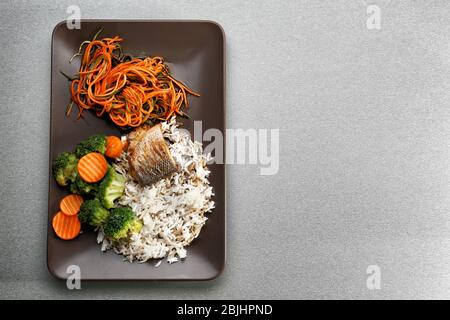 Piatto con pesce delizioso, salsa, riso e verdure sul tavolo Foto Stock