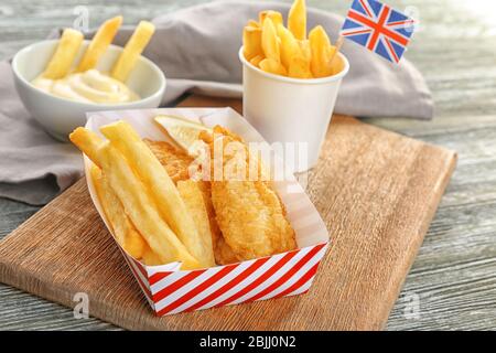 Scatola di carta con gustosi pesce fritto e patatine fritte su tavolo di legno Foto Stock