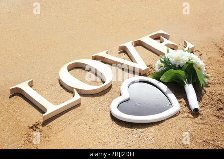 Parola AMORE composto da lettere di legno, bouquet bello e lavagna a forma di cuore sulla sabbia. Concetto di matrimonio in spiaggia Foto Stock