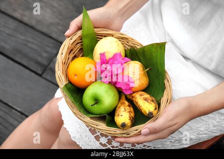 Giovane donna che tiene ciotola di vimini con frutta fresca all'aperto Foto Stock