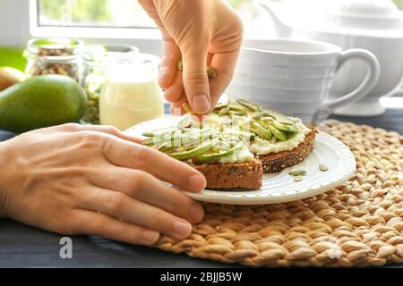 Giovane donna che prepara deliziosi toast con avocado e semi di zucca sul piatto Foto Stock