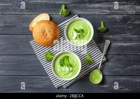Composizione con deliziosa zuppa di broccoli in ciotole su fondo ligneo Foto Stock