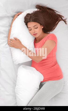 Giovane donna incinta che dorme sul cuscino di maternità nel letto Foto Stock