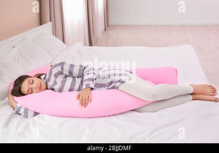 Giovane donna incinta che dorme sul cuscino di maternità a casa Foto Stock