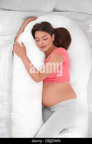 Giovane donna incinta che dorme sul cuscino di maternità nel letto Foto Stock