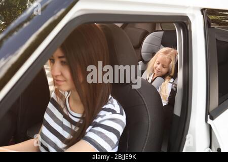 Giovane donna che guida auto con piccola ragazza in sedile di sicurezza Foto Stock