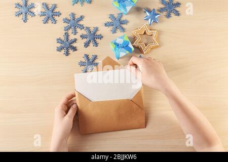 Donna che mette lettera di Natale in busta a tavola di legno Foto Stock