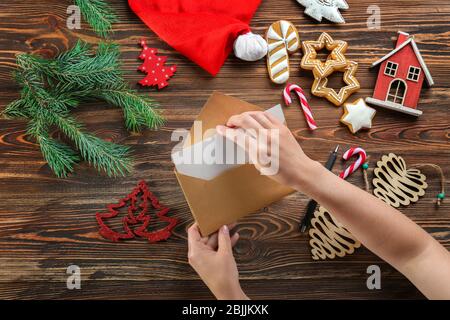 Donna che mette lettera di Natale in busta a tavola di legno Foto Stock