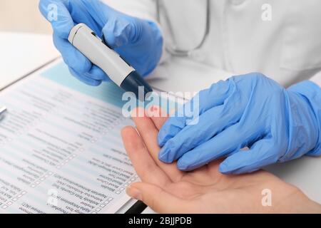 Tecnico medico in guanti di lattice che preleva campioni di sangue del paziente con penna a lancetta in ospedale Foto Stock