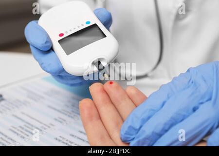 Tecnico medico in guanti di lattice che verifica il livello di glucosio del paziente con glucometro digitale in ospedale Foto Stock