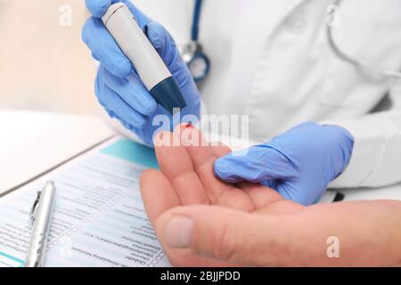 Tecnico medico in guanti di lattice che preleva campioni di sangue del paziente con penna a lancetta in ospedale Foto Stock