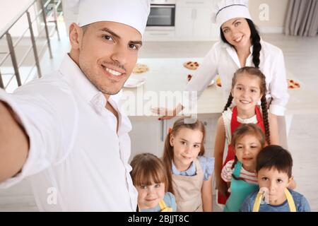 Due chef e bambini carini che prendono selfie dopo le lezioni di cucina Foto Stock