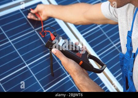 Giovane lavoratore che controlla l'installazione dei pannelli solari utilizzando un multimetro Foto Stock