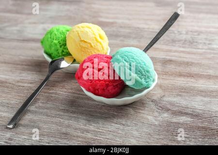 Composizione con scoop colorati di gelato e cucchiai su sfondo legno Foto Stock