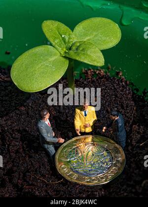 Un nuovo sparo verde con una moneta da libbra e 3 figurine in miniatura su uno sfondo di suolo Foto Stock