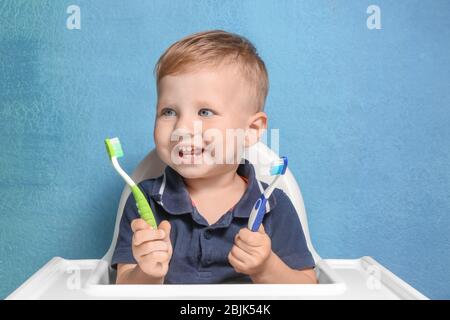 Adorabile ragazzino che tiene due spazzolini su sfondo colorato Foto Stock