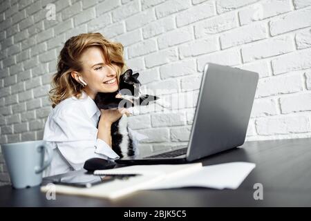 Donna sorridente con gatto nero tra le braccia seduto al tavolo con il laptop. Freelance. Foto Stock