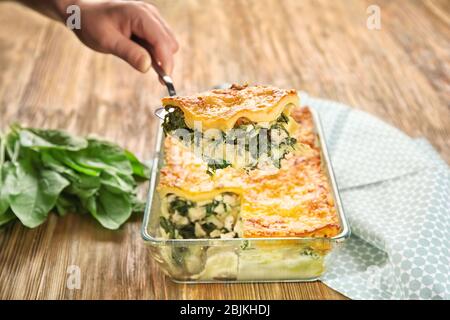 Donna che tiene spatola con pezzo di spinaci lasagne su vassoio da forno Foto Stock