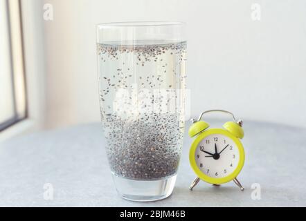 Bicchiere d'acqua con semi di chia e sveglia sul davanzale Foto Stock