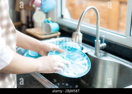 Chiudi mano di giovane donna asiatica attraente è lavando piatti al lavandino della cucina mentre facendo la pulizia a casa durante il soggiorno a casa utilizzando il tempo libero ab Foto Stock