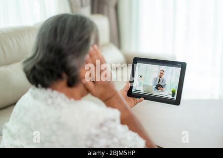 Vista posteriore della donna anziana che fa videochiamata con il suo medico con la sua sensazione di mal di testa sul tablet digitale online assistenza sanitaria tecnologia digitale Foto Stock