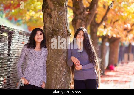 Due ragazze o giovani donne biraciali in piedi accanto all'albero di acero con foglie d'autunno colorate Foto Stock