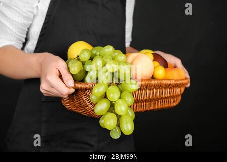 Donna che tiene cesto di vimini con frutta fresca su sfondo nero Foto Stock