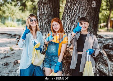 Amici che raccolgono rifiuti dal parco. Le ragazze mostrano il pollice in su. Foto Stock