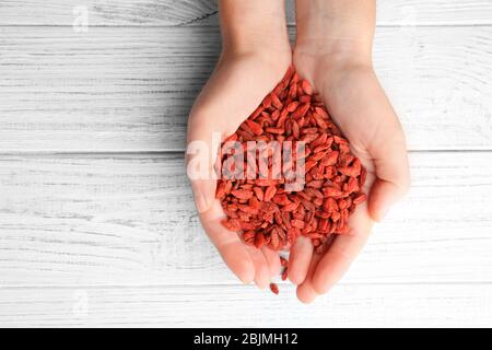 Mani di donna che tiene rosso bacche di goji asciutte su sfondo di legno Foto Stock
