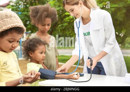 Medico volontario che misura la pressione sanguigna del bambino africano povero all'aperto Foto Stock