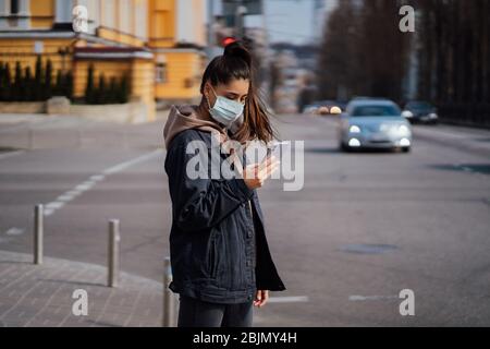 Ragazza con maschera protettiva che usa lo smartphone all'aperto. COVID 19. Pandemia mondiale di coronavirus. Foto Stock