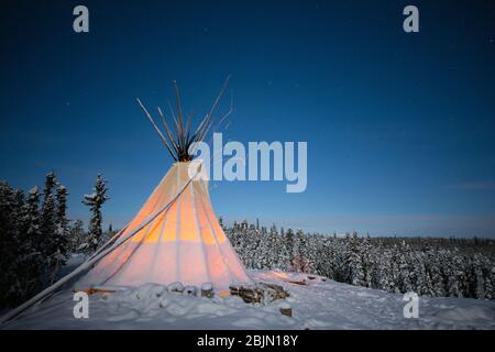 Teepee incandescente nella foresta invernale di notte, Yellowknife, territori del Nord-Ovest, Canada Foto Stock