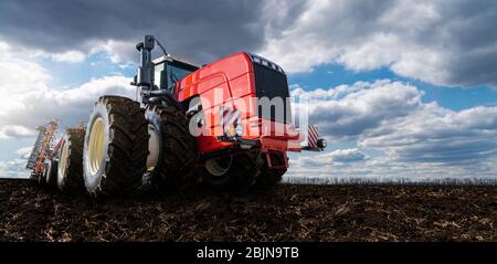 Trattore rosso con aratro su un campo agricolo Foto Stock