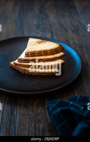 Fette di formaggio affumicato piccante Circassiano Triangle su piatto di legno scuro con spezie. Pronto a mangiare. Foto Stock