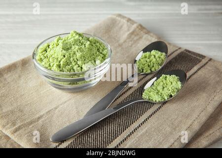 Polvere di erba di grano in ciotola e cucchiai su tavola Foto Stock