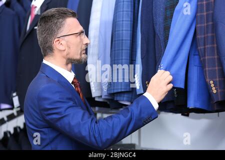 Uomo bello che sceglie il vestito in negozio Foto Stock